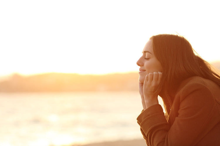 Blog of What Is Brain Retraining? 7 Things to Expect When You Start which have image A young woman with long hair and a serene expression rests her chin on her hands while facing the golden sunset at the beach. 
