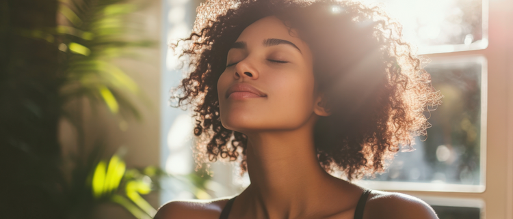 Blog of The Best Hair Growth Vitamins for Longer, Thicker, Shinier Hair which have image A young woman with curly hair basks in sunlight, eyes closed and serene.