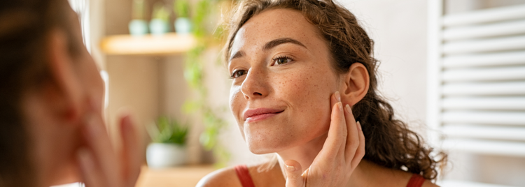 Blog of The Gut-Skin Axis: How Your Gut Health Impacts Breakouts and Aging Skin which have image Woman examining her skin in the mirror